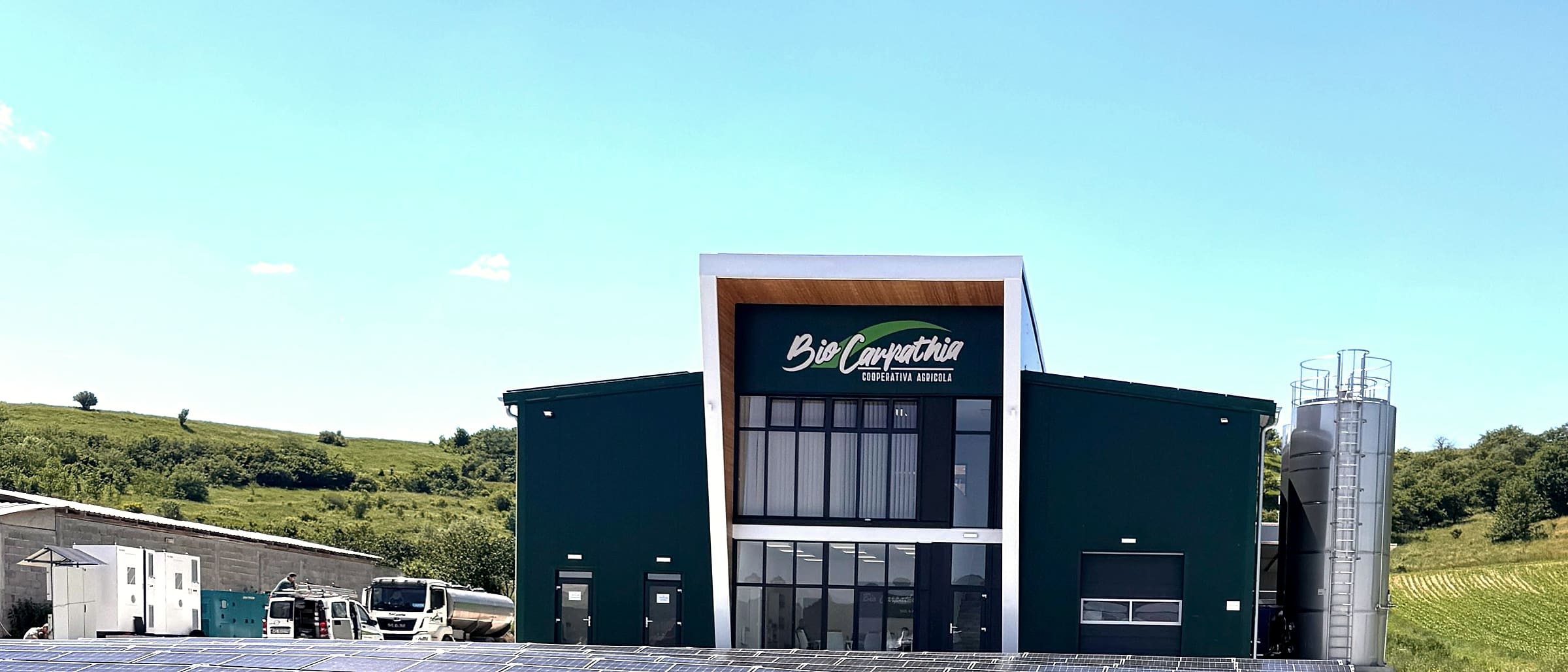 Unitatea Bio Carpathia din Măieruș, cu panouri fotovoltaice pe acoperiș și dealuri în spate